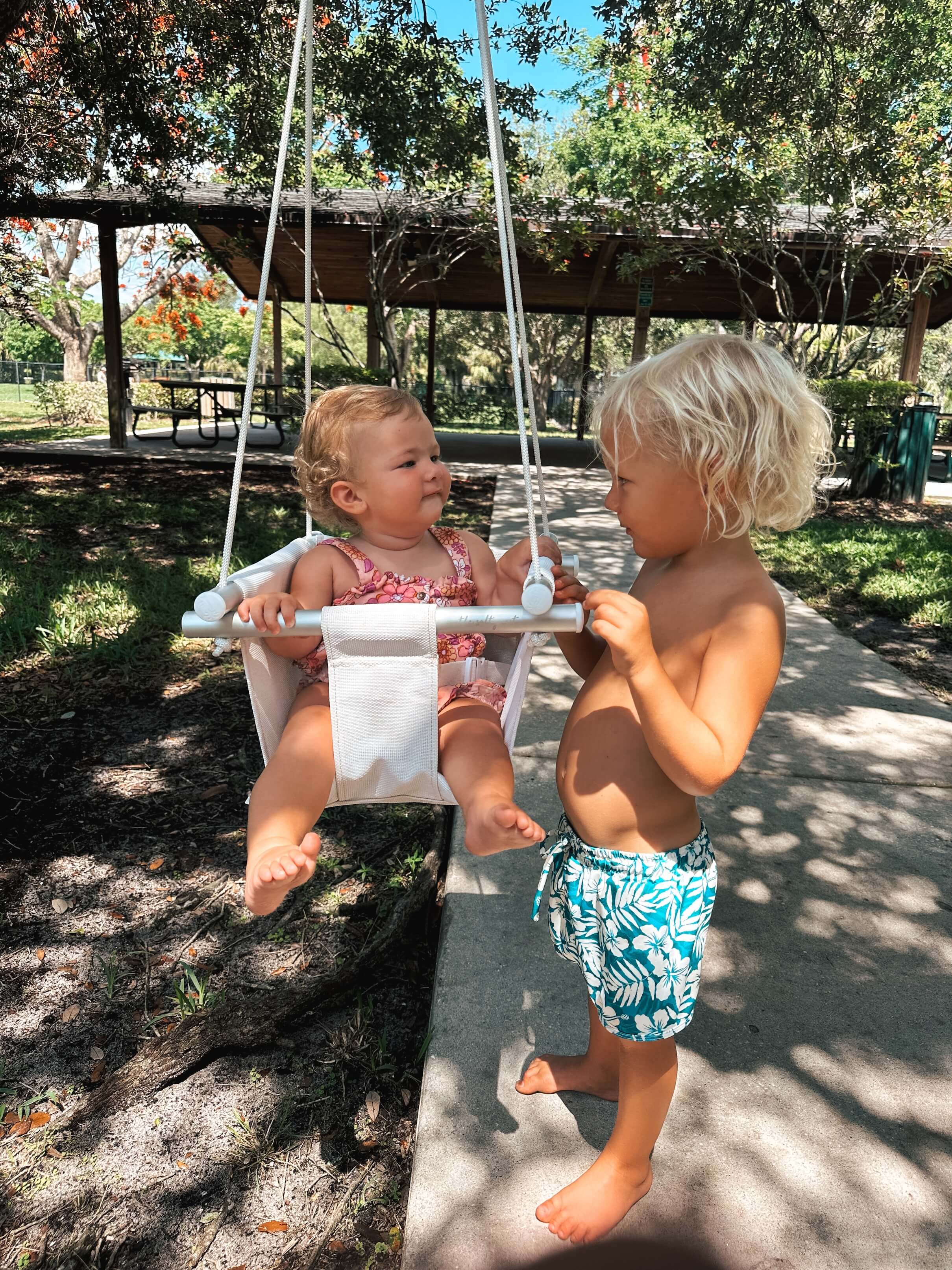 Two children playing on a Salty Nest baby swing set in a park.