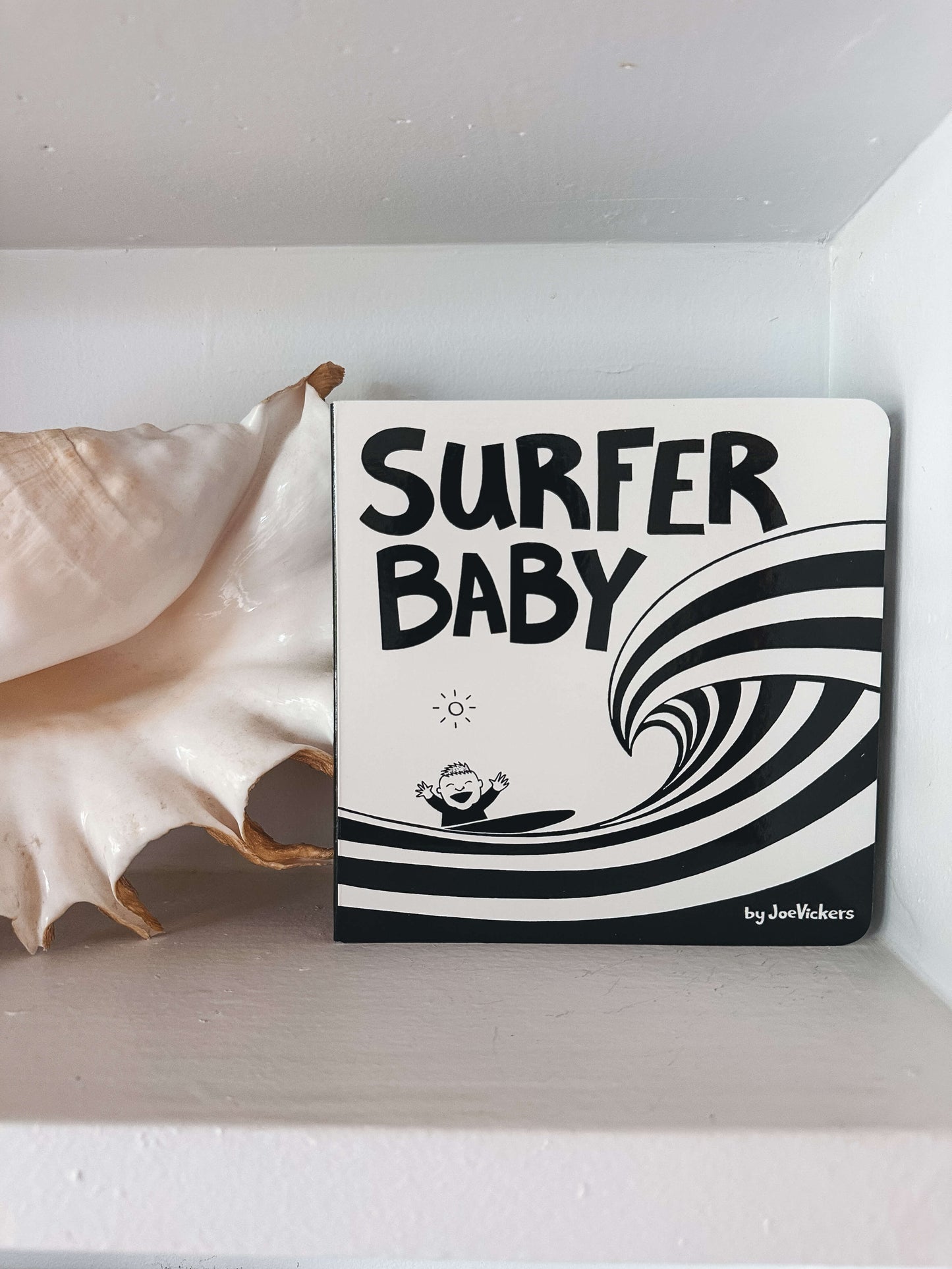 Hardback 'Surfer Baby' book on a white surface with a shell