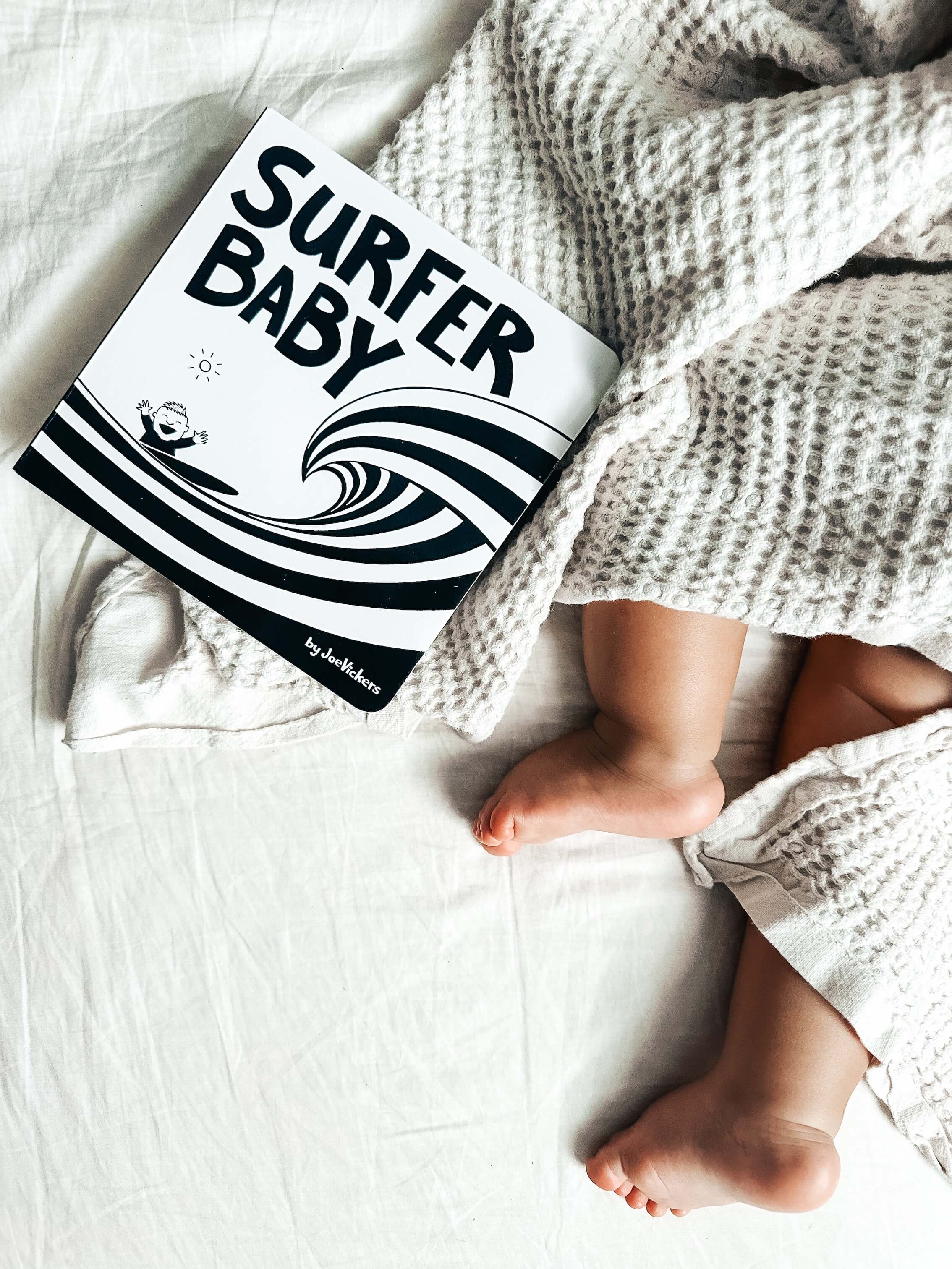 Baby blanket with 'Surfer Baby' and wave design, draped over a baby's legs.